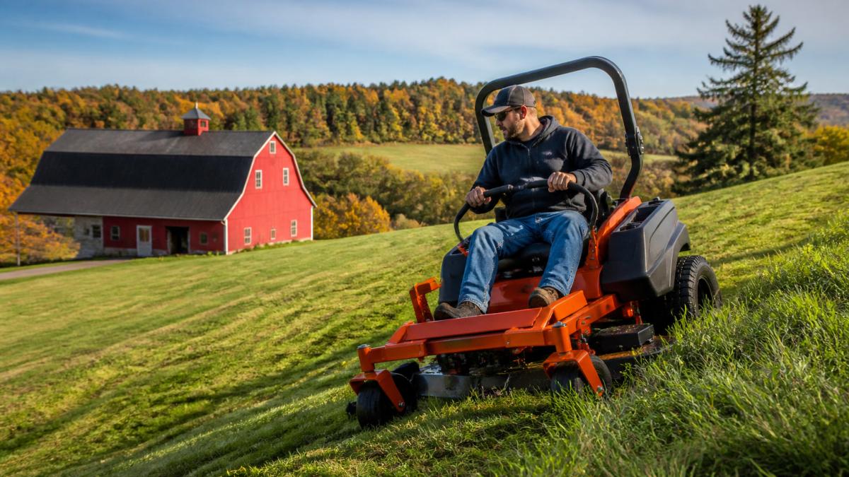 Homeowner operating a Bad Boy zero turn mower on a sloped Western New York lawn with a red barn in the background