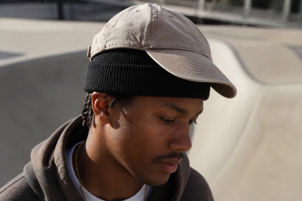 Close-up van iemand die een vintage gewassen beige cap en zwarte beanie draagt, gestapeld op het hoofd, met streetwear outfit in natuurlijk daglicht