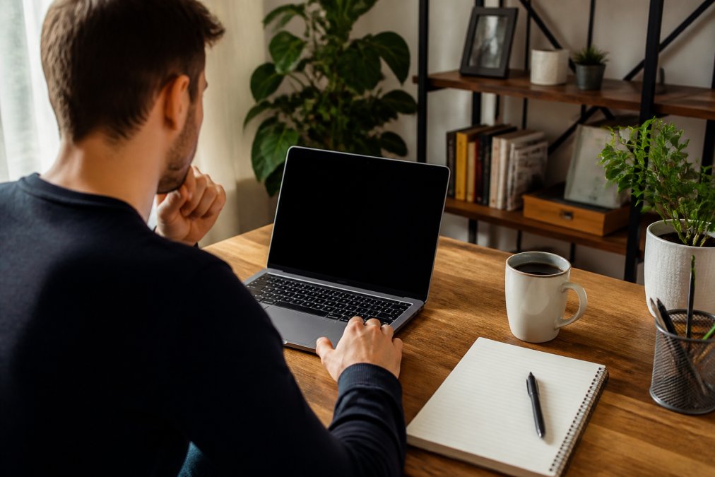 A person sitting at a tidy home office desk comparing hosting options on a laptop screen, with a notepad and coffee cup nearby, warm natural light