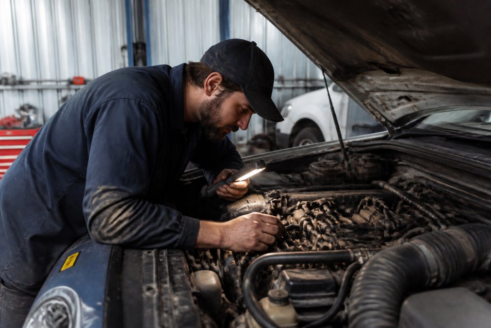 A mechanic in a dusty Mildura workshop inspecting the open bonnet of a diesel 4WD, checking the fuel lines and glow plug wiring with a work light