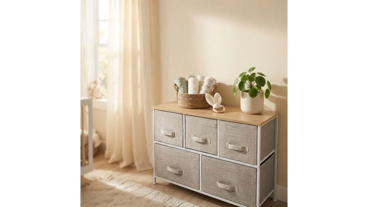 A softly lit nursery corner with a wooden dresser, folded baby clothes in fabric drawers, and a changing mat on top, showing a calm and organised space