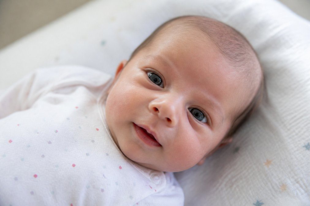 Close-up of newborn baby's face showing alert expression and eye contact, with soft natural lighting from window