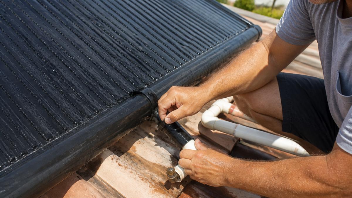 Technician inspecting a leaking header on a solar pool heating sensor panel on a roof
