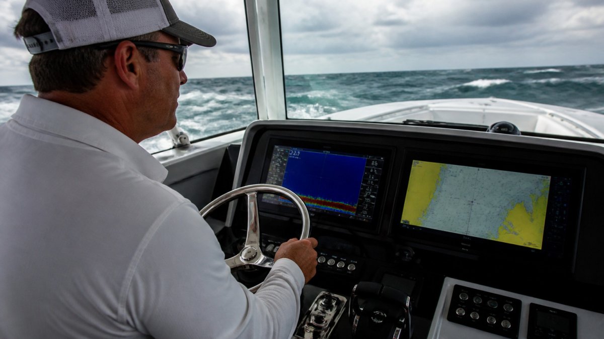 Captain at the helm using a chartplotter to evaluate yacht navigation electronics during an offshore sea trial.