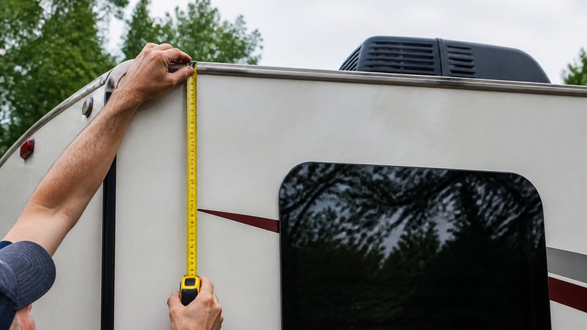 Homeowner using a tape measure to measure rv carport height at the motorhome roof edge.