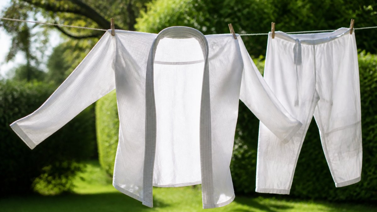 Natte BJJ-gi die binnenstebuiten aan een waslijn buiten aan de lucht droogt in zonnig weer, met groene achtergrond