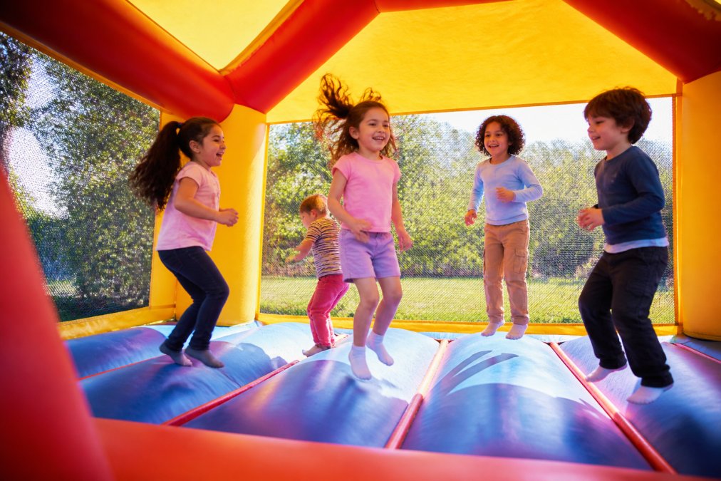 A group of children laughing and jumping inside a colorful bounce house at an outdoor birthday party on a sunny day
