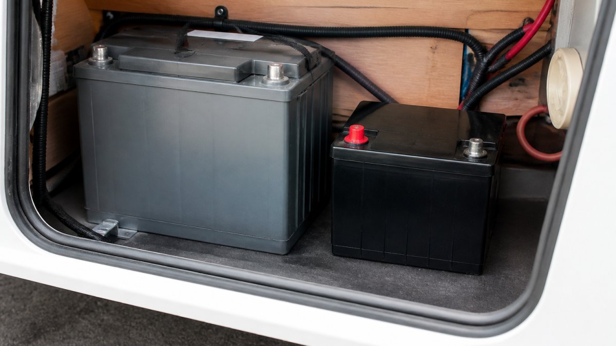 Kompakte Lithium-Batterie neben größerer AGM-Batterie in Wohnwagen-Batteriefach, um Größenunterschiede deutlich zu zeigen