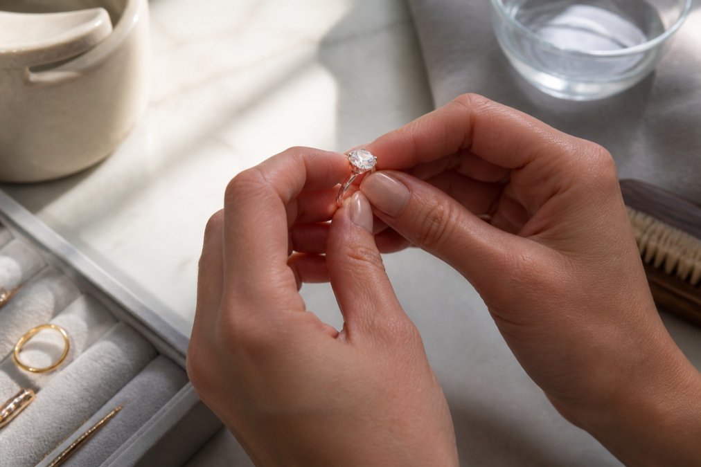 Close-up of hands holding an engagement ring under soft natural light, examining the diamond and metal band for any visible damage or debris before cleaning