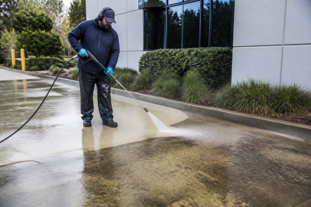 Technician using a pressure washer to clean stained concrete for 5 ways to improve commercial property curb appeal