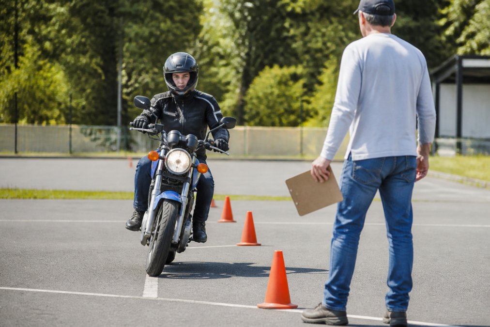 Young rider in protective helmet and gear practicing controlled braking maneuver on motorcycle during hands-on training course in outdoor practice lot with clear markings