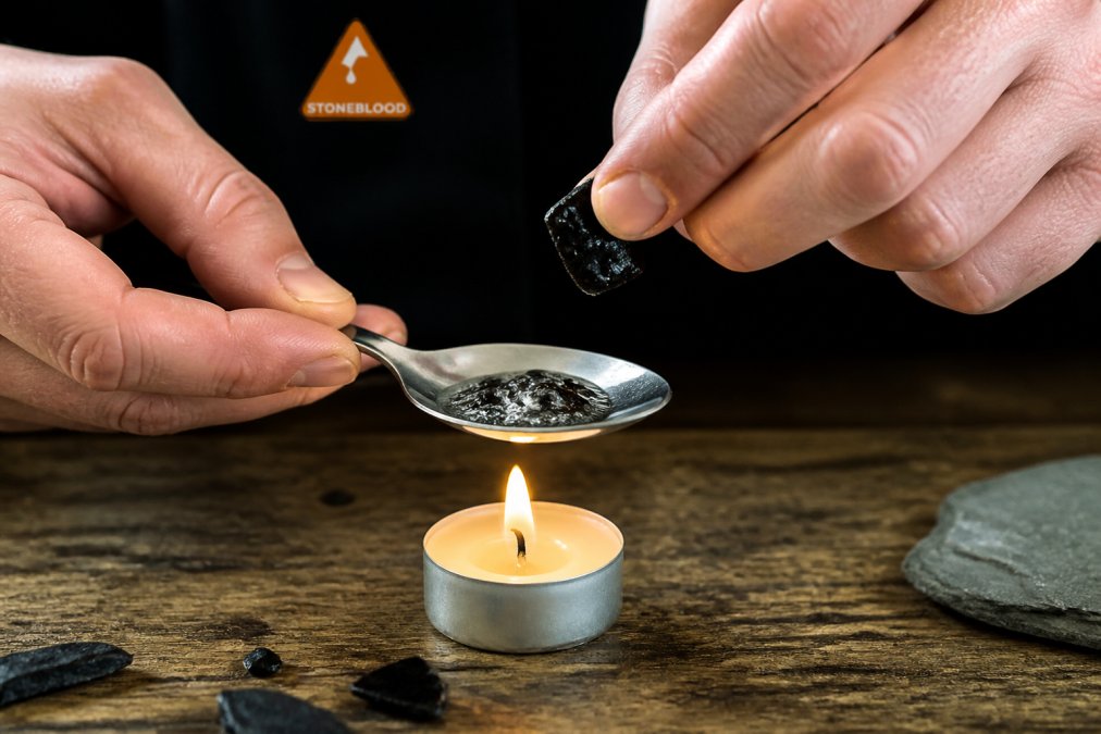 Process of testing fake shilajit resin by observing how it bubbles when heated over a candle flame on a spoon.