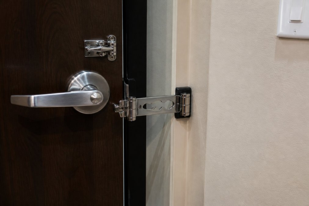 Close-up of a hotel room door with a portable door lock device installed on the frame, showing the chrome-plated mechanism securing the door from inside