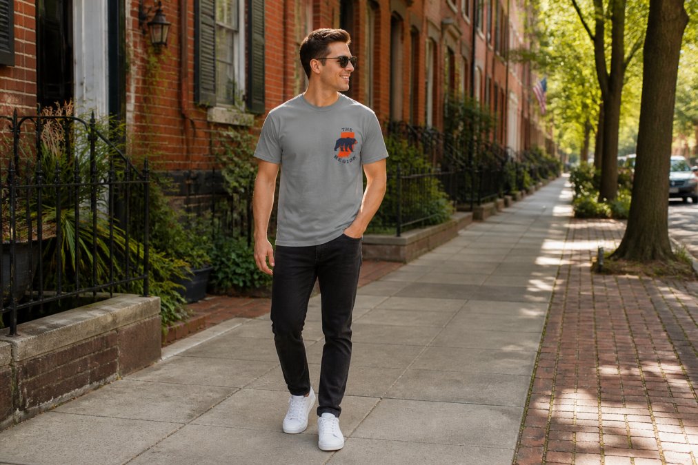 Person wearing a regional pride t-shirt styled casually with dark jeans and white sneakers, standing outdoors in an urban neighborhood setting with brick buildings and natural afternoon lighting