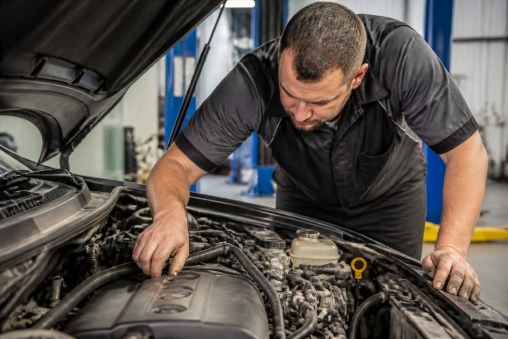 Skilled mechanic inspecting under the bonnet of a vehicle using modern diagnostic equipment, examining engine components with focused attention in a well-lit workshop