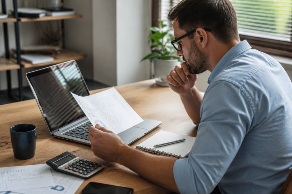 Business owner reviewing pricing strategy on computer screen with financial data visible, sitting at desk with coffee and notepad