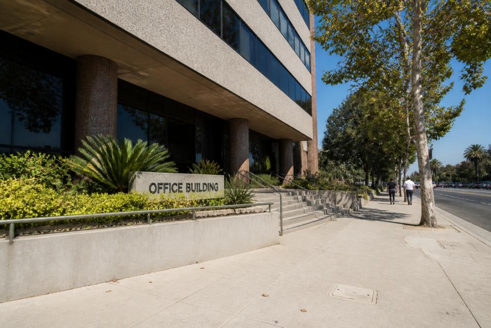 Pedestrians walk past the Van Nuys immigration court office building entrance on Van Nuys Boulevard during the day.