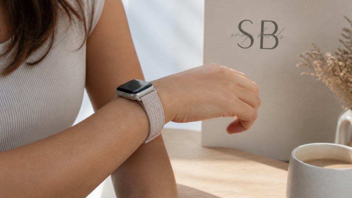 Close-up of a woman's wrist wearing a smartwatch with a soft woven nylon band, natural daylight, calm neutral background, skin calm and healthy