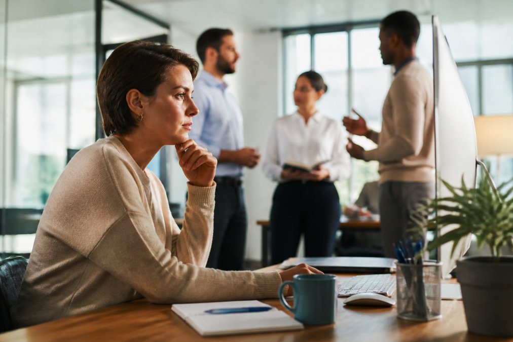 Professionnel RH ou manager examinant des métriques de performance sur un écran d'ordinateur, avec des collègues discutant des résultats de formation en arrière-plan