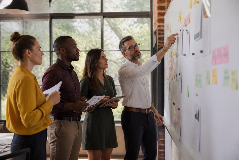 A diverse marketing team collaborating around a whiteboard covered in strategy notes and sticky notes in a bright modern office