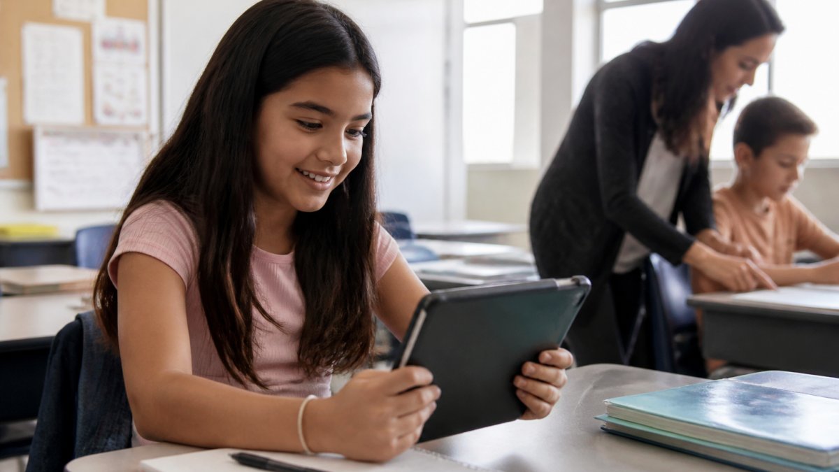 Student smiling at a tablet screen showing digital assessment results in a bright classroom with a teacher nearby.