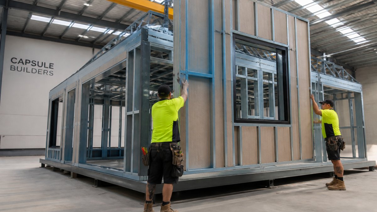 Workers assembling an eco friendly modular home wall panel in a clean factory setting