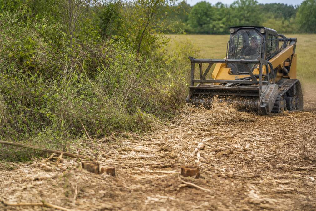 Tracked skid steer using professional land clearing equipment to mulch brush into a nutrient-rich soil layer