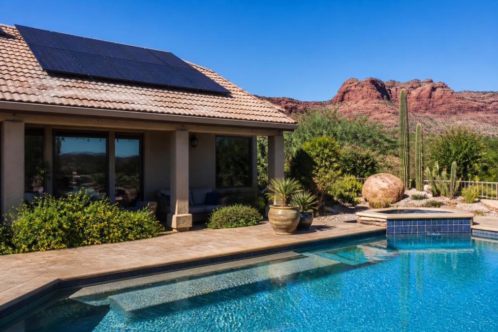 Solar panels on a roof heating a residential pool in a desert landscape to provide sustainable pool heating.