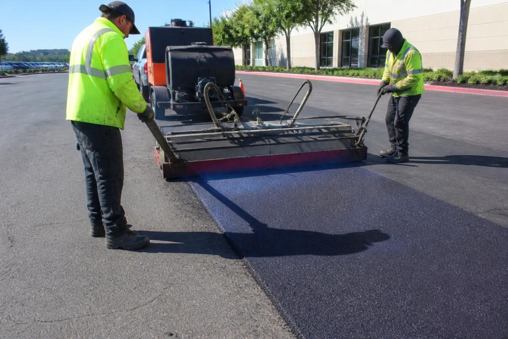 Professional paving crew using an infrared heater to soften existing asphalt on a commercial parking lot, showing the seamless blend of old and new material under bright daylight