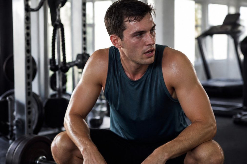 Male athlete wearing performance training tank during intense workout, demonstrating sweat management and athletic fit in action with natural gym lighting