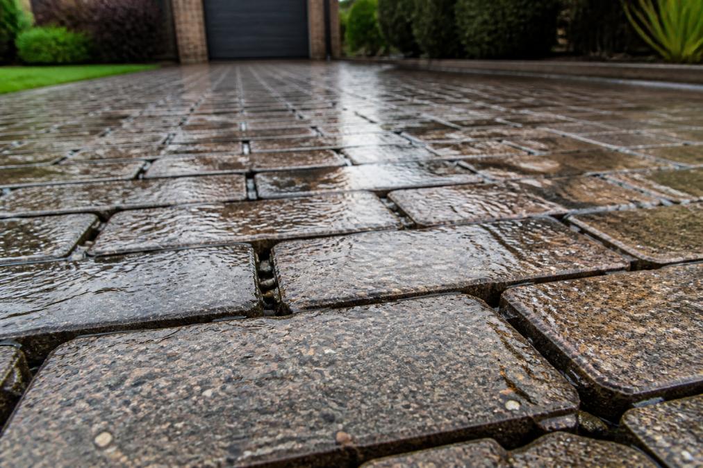 Close-up view of permeable block paving installed on a residential driveway in Norfolk, showing water draining through the blocks during light rain, with visible gaps between blocks allowing water infiltration