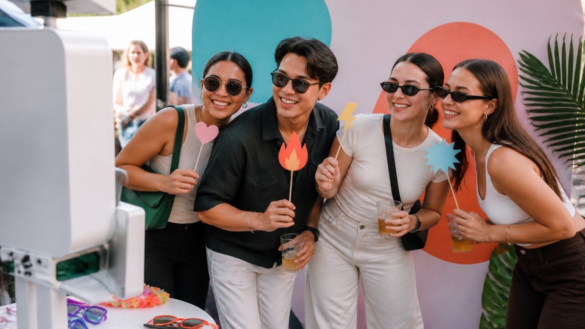 Diverse group of event attendees smiling and engaging at a branded activation booth with custom backdrop and props, capturing moments together