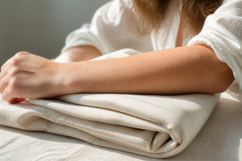 Close-up of a person's forearm with calm, healthy skin resting on a folded light-colored cotton fabric in soft natural sunlight