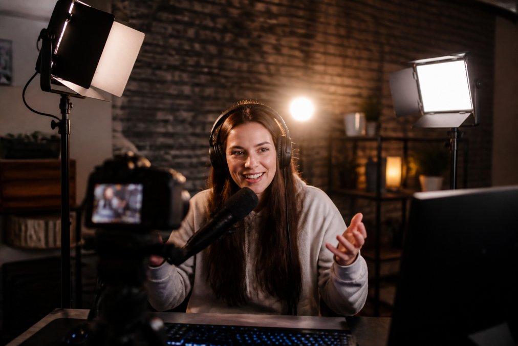 Professional streamer at gaming desk with three distinct light sources positioned around them, key light at 45 degrees to the left, fill light softening shadows on the right side of face, and backlight creating rim light separation from the background wall