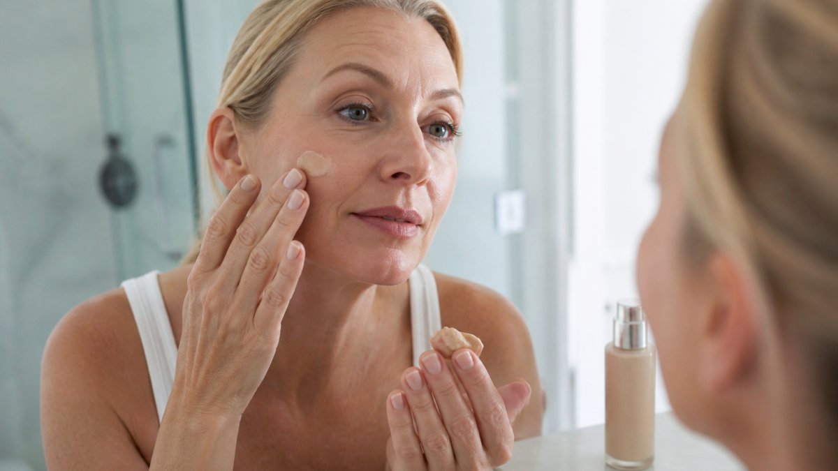 Woman in her fifties applying tinted mineral sunscreen to her cheek in a bright bathroom setting