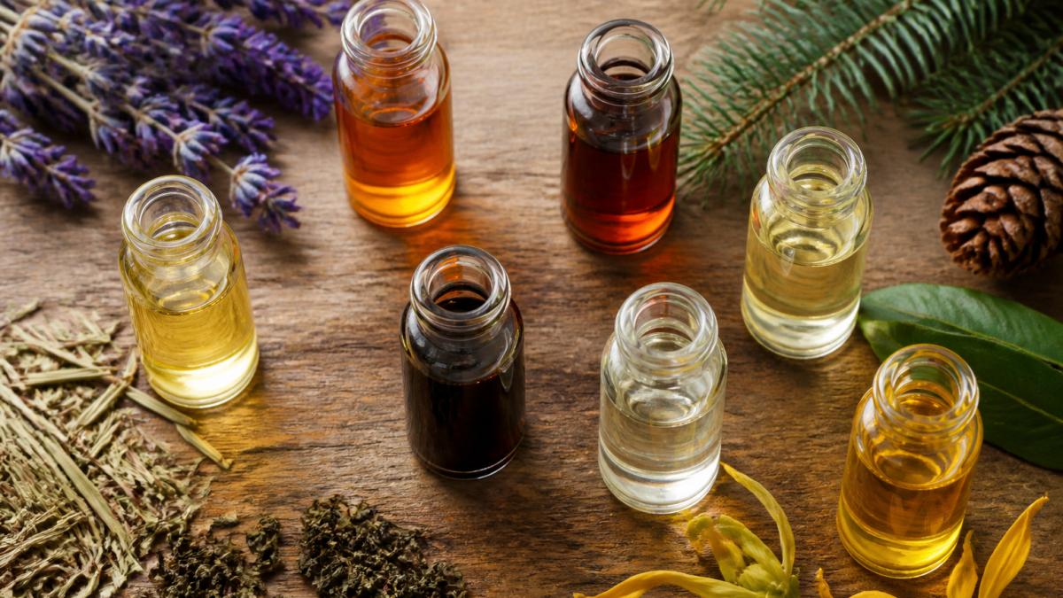 Seven glass bottles of essential oils with fresh botanicals as the 7 best natural oils for cold process soap.