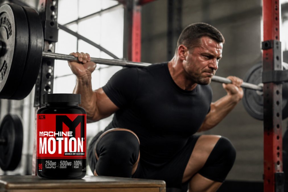 Athlete performing heavy barbell squat with intense focus, sweat visible on face and arms, showing the physical demands placed on joints during strength training in a bright gym setting