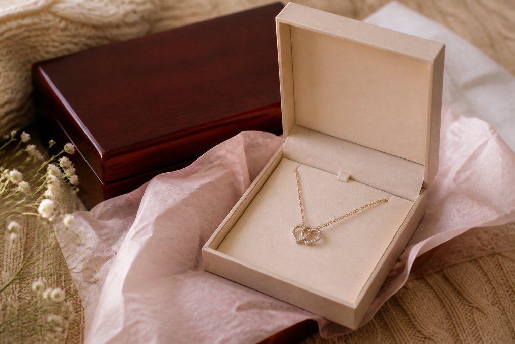 Elegant gift box with soft touch packaging containing a personalized necklace, with tissue paper and mahogany luxury box visible in the background, photographed in warm natural light
