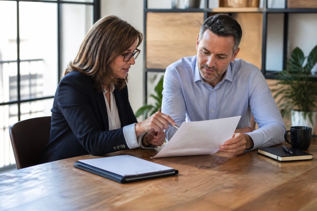 A marketing executive and business founder reviewing a printed onboarding checklist together at a wooden conference table in a bright office