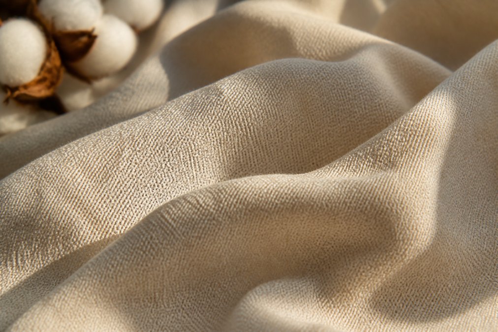 Close-up of organic cotton fabric texture showing natural fiber weave and breathability, with soft natural sunlight highlighting the delicate threads and organic structure