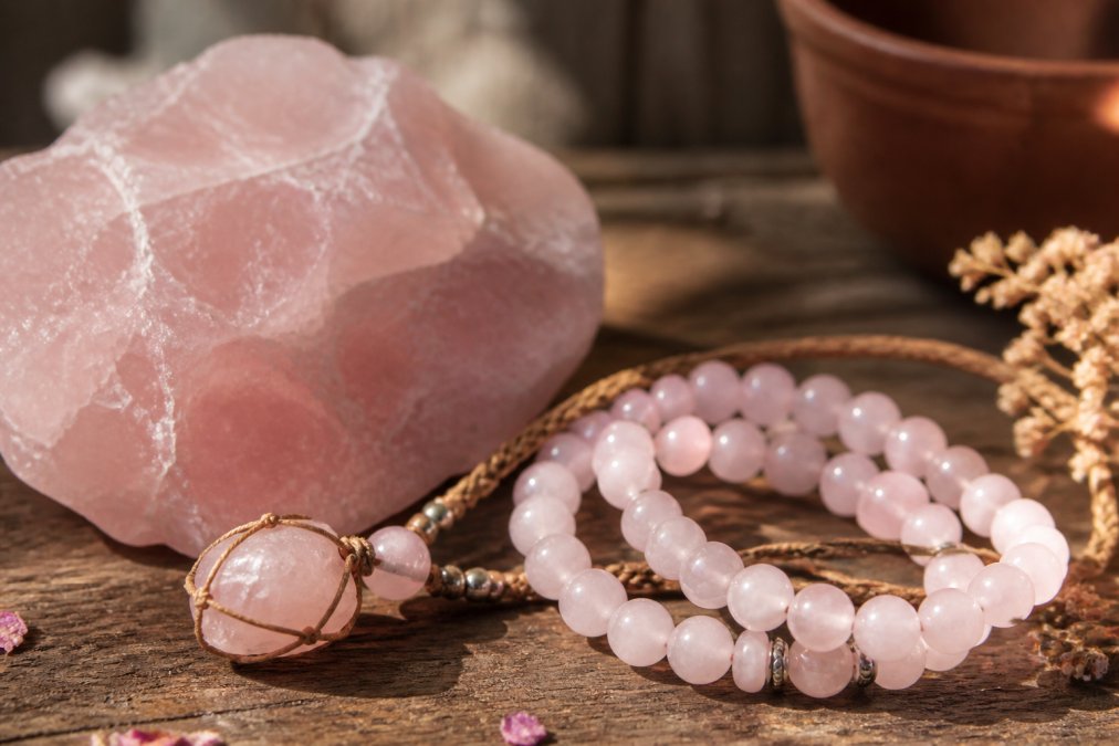 Close-up van rozenkwarts armbanden en kettingen met natuurlijke rozenkwarts stenen in warm daglicht, gedrapeerd op een houten oppervlak met rustieke achtergrond