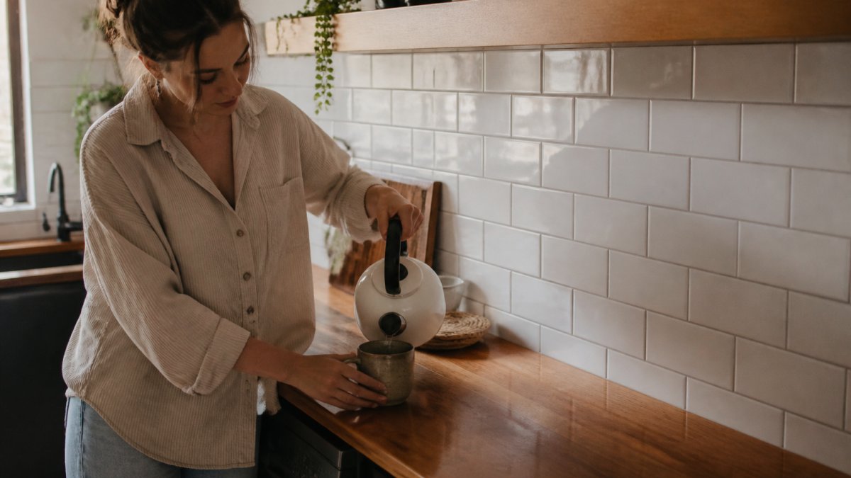 Close-up of a freshly tiled kitchen splashback in white subway tiles with a timber benchtop and a kettle in soft natural light
