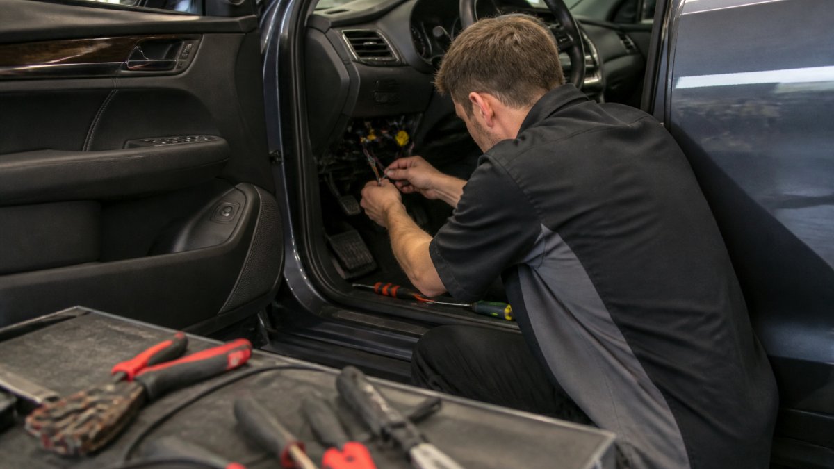 Automotive technician routing wiring under a dashboard during a professional car starter installation