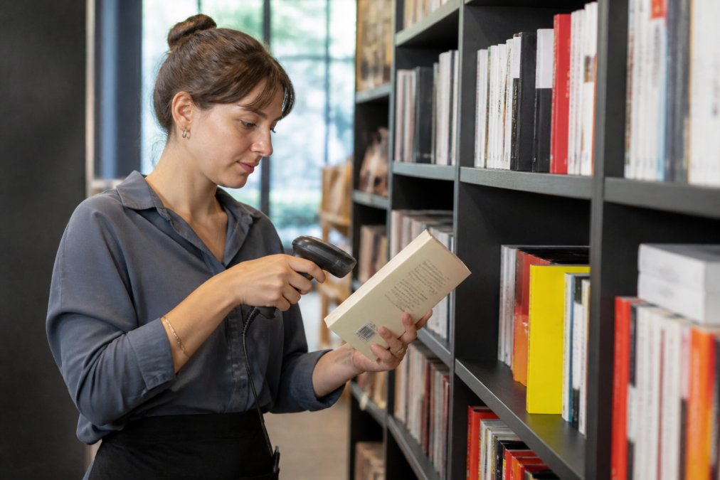 Librario scansiona il codice a barre di un libro per la gestione magazzino libreria tra gli scaffali ordinati