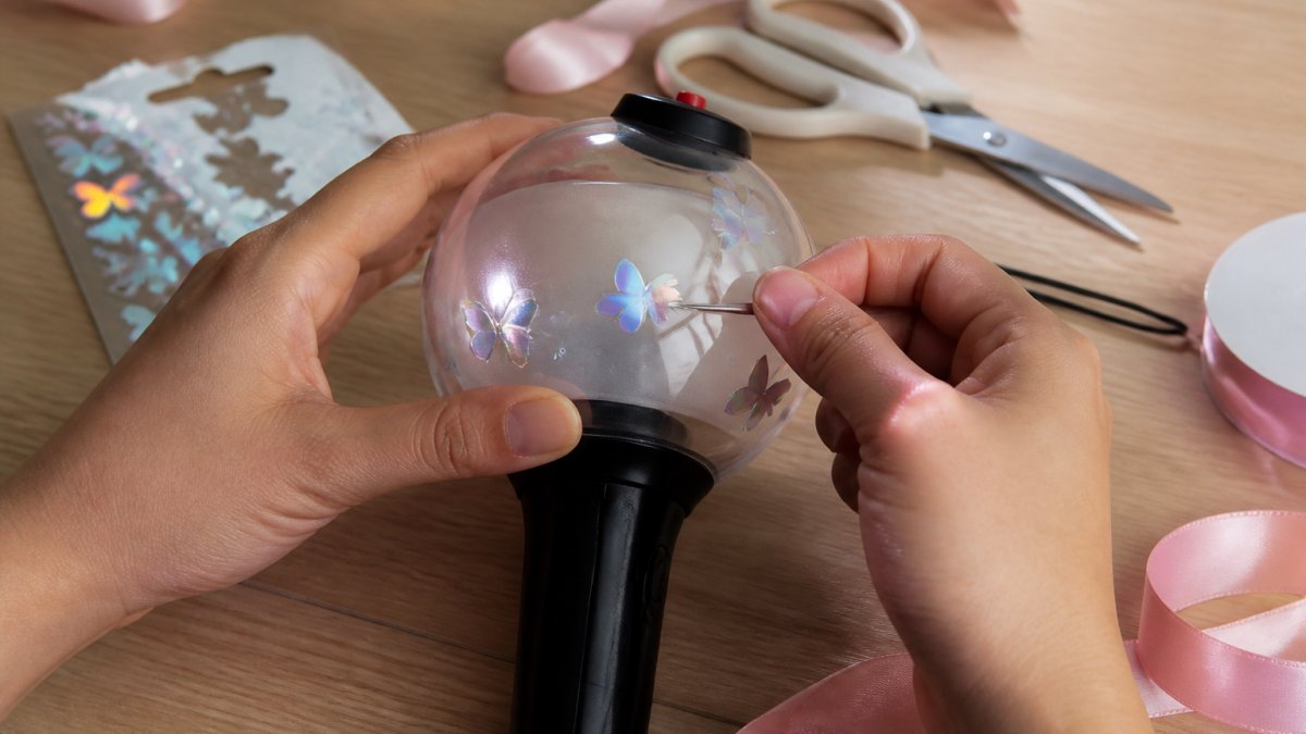 Step-by-step guide for applying a vinyl decal to a spherical lightstick using craft tools and ribbon decor