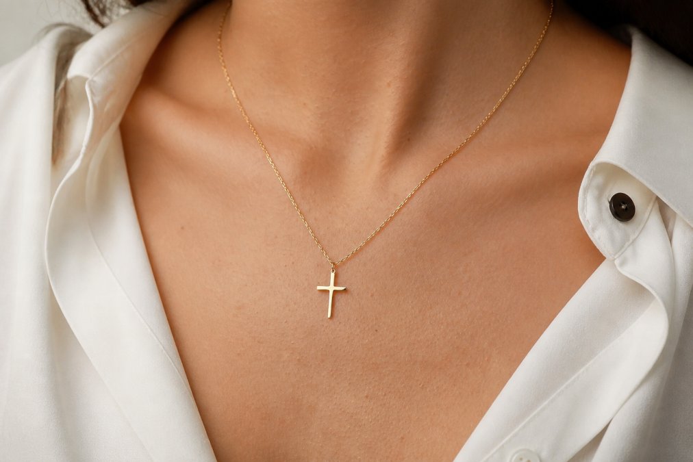 Woman wearing a delicate gold-plated cross necklace at her collarbone in natural daylight, showing how the pendant sits against her chest and the chain drapes along her shoulder