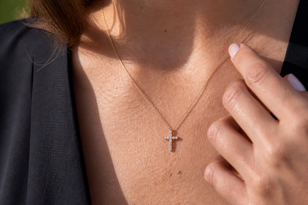 Woman wearing a sparkling CZ stone cross necklace against her collarbone in bright natural daylight, showing how the cubic zirconia stones catch and reflect light
