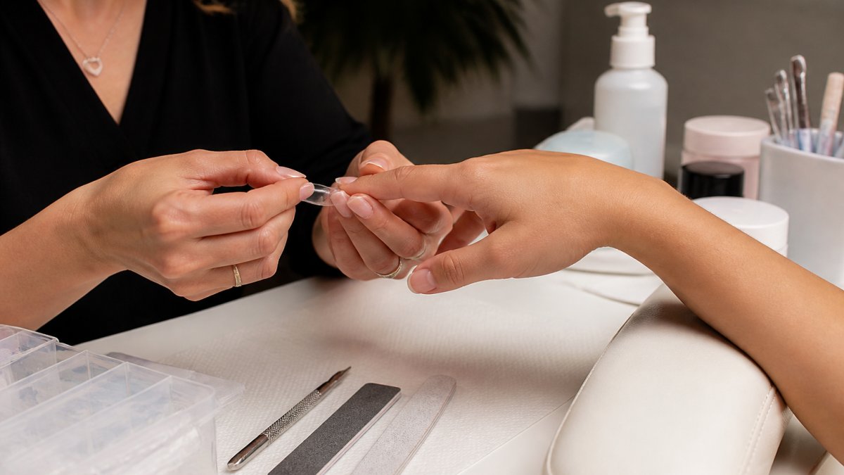 Nail technician applying a soft gel-x nail extension tip to a client’s natural nail in a quiet studio