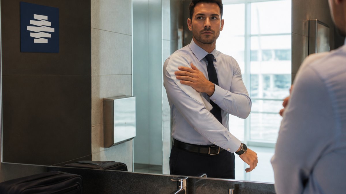 Professional in business attire freshening up with an oversized body wipe in an airport bathroom, natural lighting from mirror, composed and ready for next meeting
