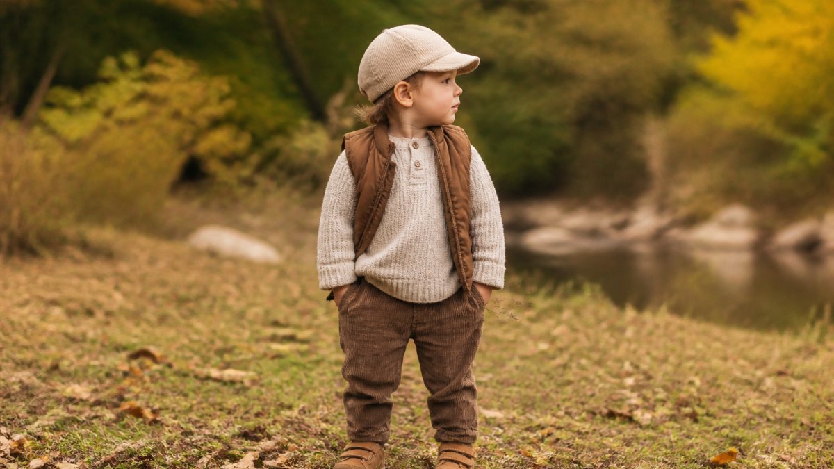 Child in a neutral cap and textured fall layers posing outdoors during a kids accessories photo shoot